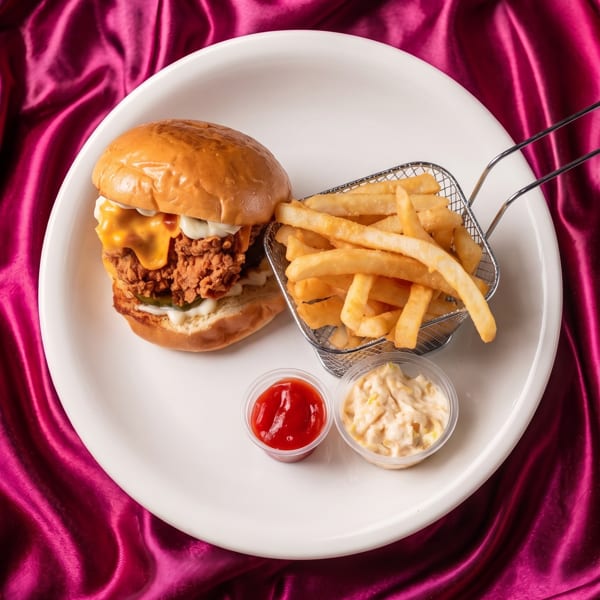 Crispy chicken burger with melted cheese, fries in a mini basket, ketchup, and coleslaw on a white plate.