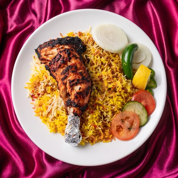 Grilled chicken leg with rice, sliced onions, jalapeños, lemon, tomatoes, and cucumbers on a white plate.