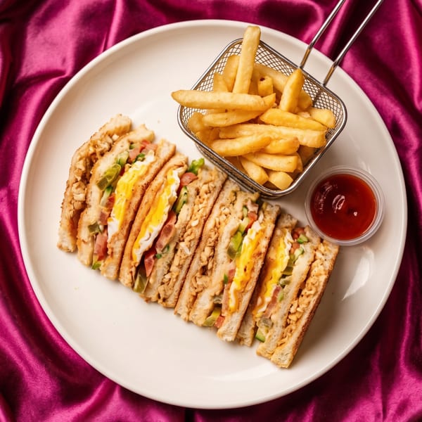 Club sandwiches with fried eggs and vegetables, served with fries and ketchup on a white plate.