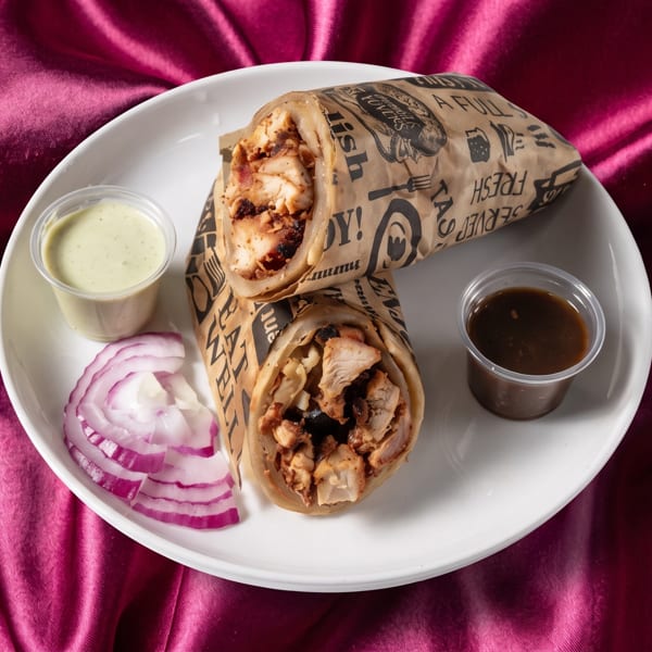Two chicken wraps on a white plate with sliced red onions and two dipping sauces, on a magenta satin background.